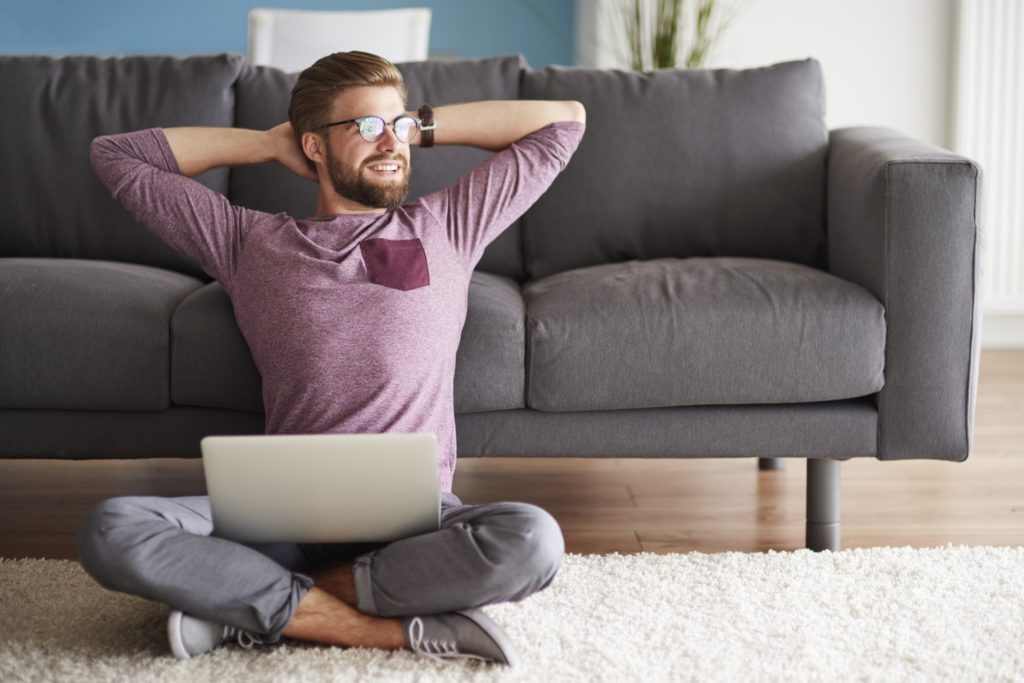 Young Man Working from home sitting on floor hands behind head stretching